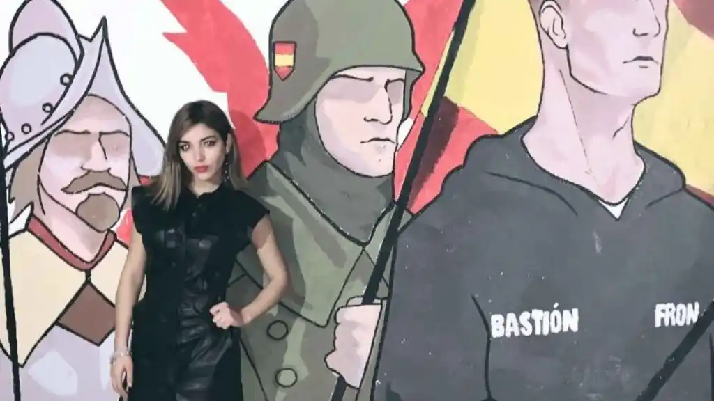 Isabel Medina Peralta, figura de la extrema derecha española, posa frente a un mural con soldados y símbolos asociados al grupo ultranacionalista Bastión Frontal. La imagen resume la estética militarizada y el revisionismo histórico que acompañan al discurso neofalangista.