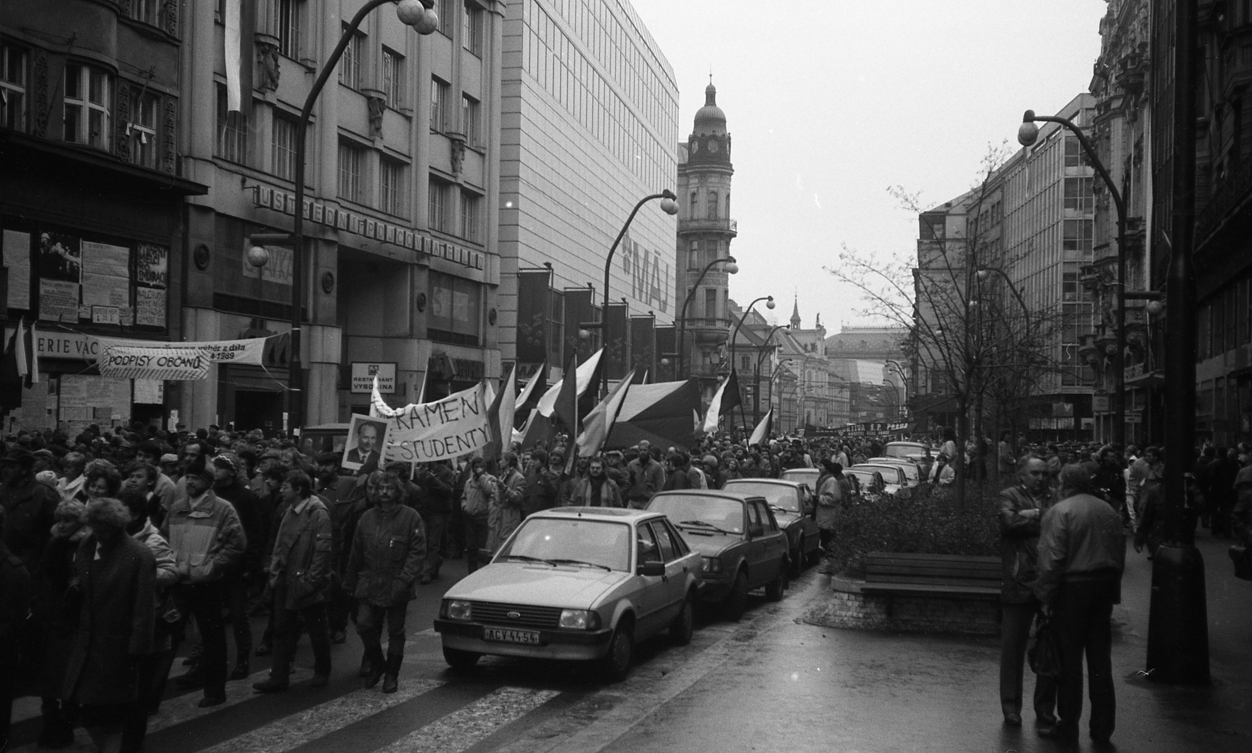 Protest march during the Velvet Revolution in Prague, with citizens carrying banners and flags on a crowded street, November 1989.